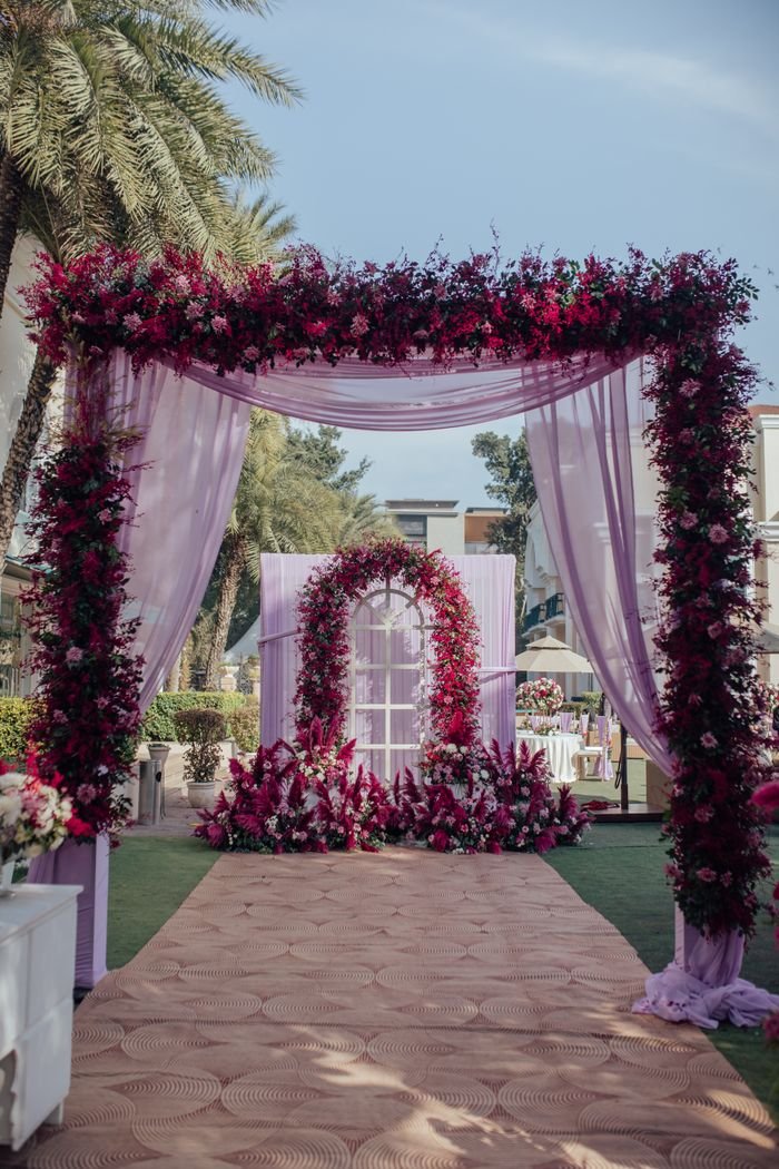 A beautiful wedding arch adorned with vibrant flowers set in a sunlit outdoor garden.